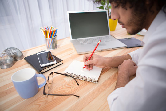 Closeup of man writing something in notebook or diary while sitting at wooden table. Hipster freelance man working at home. Business concept.