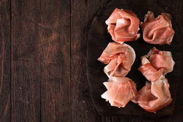 Slices of Prosciutto on old wooden background.