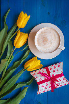 Coffee mug with yellow tulip flowers,gift and notes good morning on blue rustic table from above, breakfast on Mothers day or Womens day .Spring  flowers bouquet