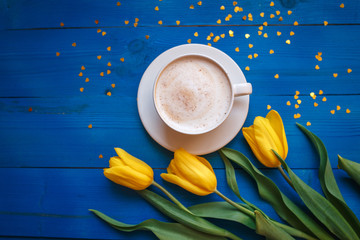 Coffee mug with yellow tulip flowers and notes good morning on blue rustic table from above,...