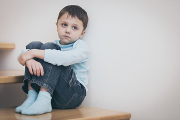 one sad little boy sitting on the stairs in house at the day time