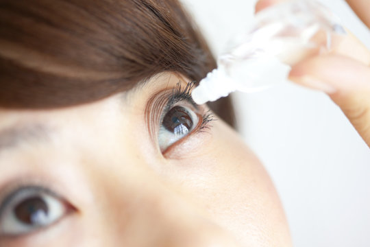 Young woman applying eye drops, close up