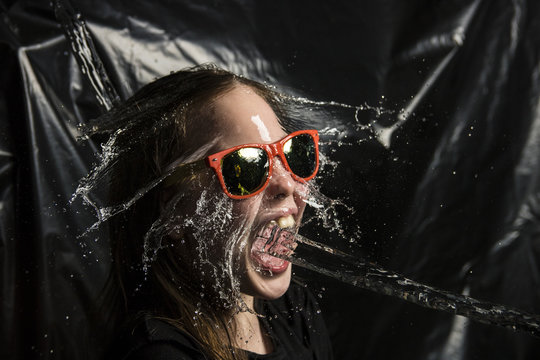 water throwing to a young girl in hands and face with black background
