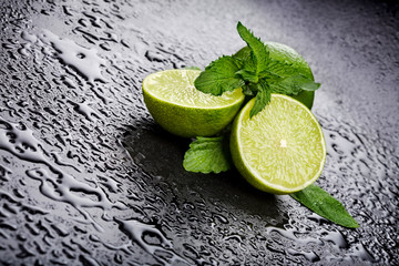 Green limes with mint and water drops on black background