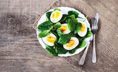 Boiled halved eggs on plate decorated with spinach leaves isolated on white. Healthy salad..