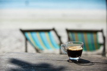 Coffee cup on wood table with sea & sand background