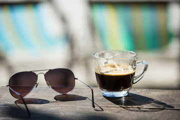 Coffee cup and Sunglasses on wood table with beach chairs & sand Background