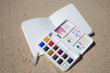 Notebook & Watercolor box on beach background