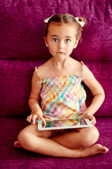 Little girl with a tablet computer on a sofa at home