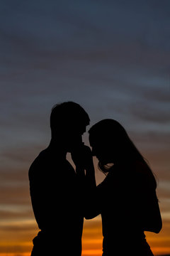 Silhouette of young couple in love on sunset sky background