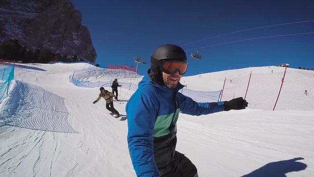 Skiing in the Alps in the winter. A man is rolling on a snowboard on the snow-covered trails of a mountain resort. The guy takes himself off on an extreme camera.