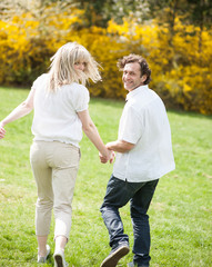 Naklejka na ściany i meble Couple holding hands with back to camera running through park