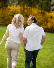 Couple holding hands with back to camera running through park