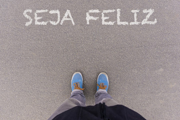 Seja feliz, Portuguese text for Be Happy text on asphalt ground, feet and shoes on floor