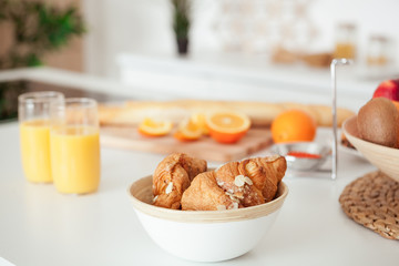Plate of tasty cookies with chocolate crumbs, croissant, baget, bananas, apples, persimmon, orange and orange juice on white table
