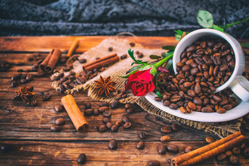 Cup filled with coffee beans on old wooden table with roses in the background.