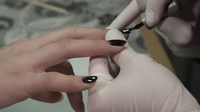 Closeup of manicure master polishing nails with the black polish