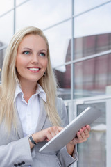 Happy businesswoman using digital tablet while looking away against office building