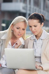 Young businesswomen working on laptop together while sitting outdoors