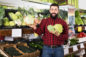 Man seller showing cauliflowers in grocery store