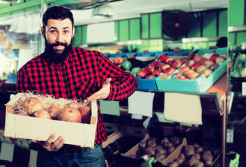Positive male seller showing pomegranates in store