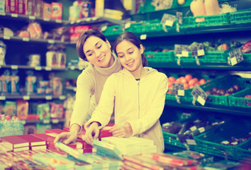 Fototapeta na wymiar smiling woman with daughter choosing cookies in supermarket