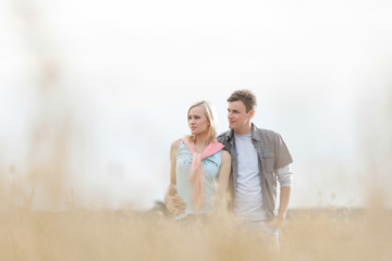 Thoughtful young couple looking away while standing at field