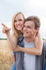 Obraz premium Happy woman showing something to man while enjoying piggyback ride at field