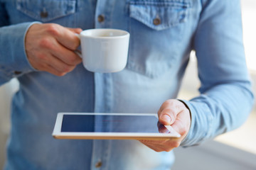 Man holding white digital tablet and cup of coffee, view close up