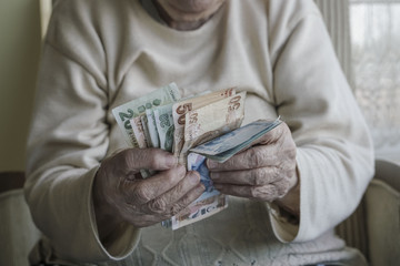 Closeup of wrinkled hands counting turkish lira banknotes