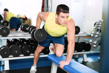 Fototapeta na wymiar Young handsome man with dumbbell training in gym