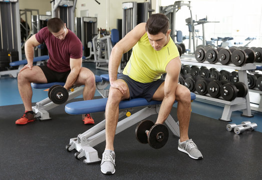 Young handsome men with dumbbells training in gym
