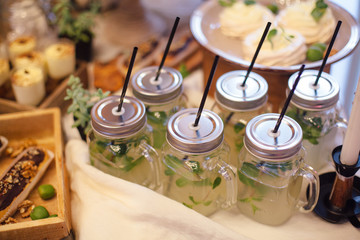 Fototapeta na wymiar Lemonade with mint in glass jar with straws in area of wedding party