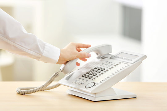 Female hand picking up telephone receiver in office