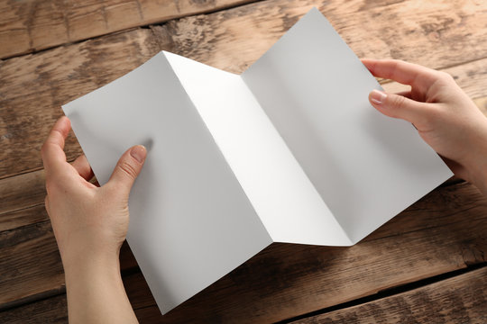 Female hands holding blank brochure on wooden background