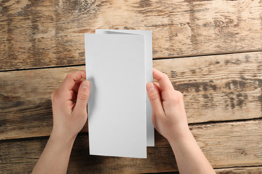 Female hands holding blank brochure on wooden background