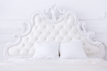 white headboard of a bed in classical style in a light bedroom