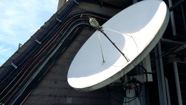 A white parabolic antenna on a wall, the blue sky in the background