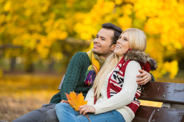 Happy young couple looking away while sitting on park bench during autumn