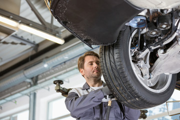 Mid adult technician repairing car's wheel in workshop