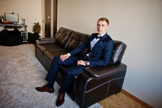 Young stylish groom sitting on leather sofa.