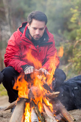 Male hiker warming his hands at campfire in forest