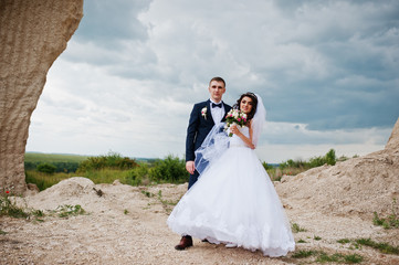 Young stylish wedding couple against sandy career at cloudy sky.