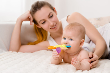 Mother and child on a white bed. Mom and baby girl in diaper playing in sunny bedroom.