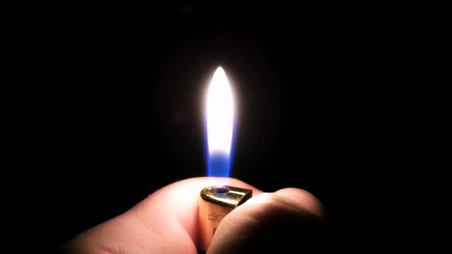 Men’s hand lights a cigarette lighter in the dark