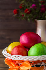Colorful painted easter eggs in basket and vase with flowers on rustic wooden table.