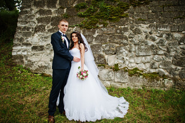 Young stylish wedding couple against old stone wall.