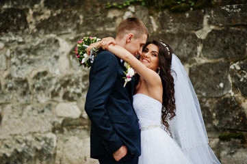 Young stylish wedding couple against old stone wall.