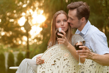 Romantic young couple having red wine on chairs in park