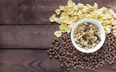 Bowl of dry muesli with corn flakes and chocolate balls on wooden background